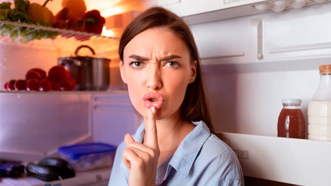 vrouw met wijsvinger voor mond voor een open koelkastdeur