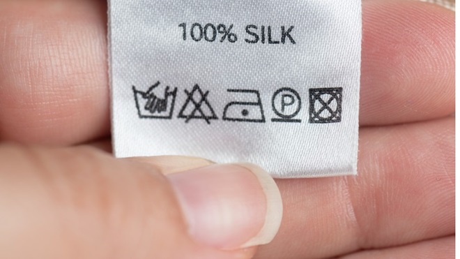 hand houdt kledinglabel met symbolen voor wassen, drogen en strijken vast