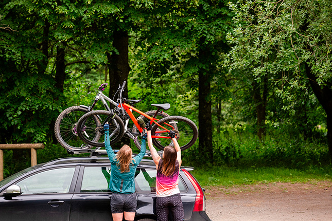 twee vrouwen tillen fiets op de fietsendrager op het dak van de auto