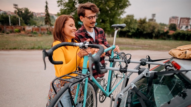 een koppel bevestigt een fiets op de fietsendrager achterop de auto