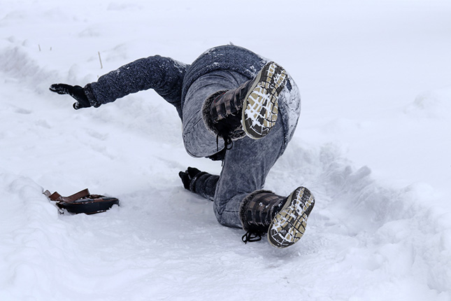 Een voetganger glijdt uit over niet geruimde sneeuw